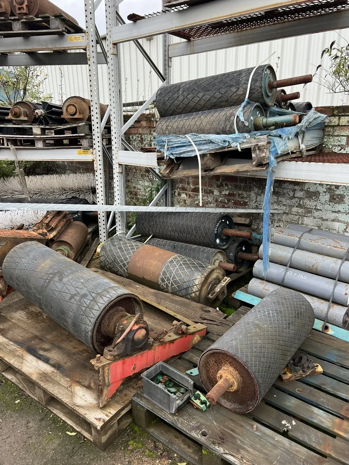 Used conveyor drums and lagged rollers racked in the yard